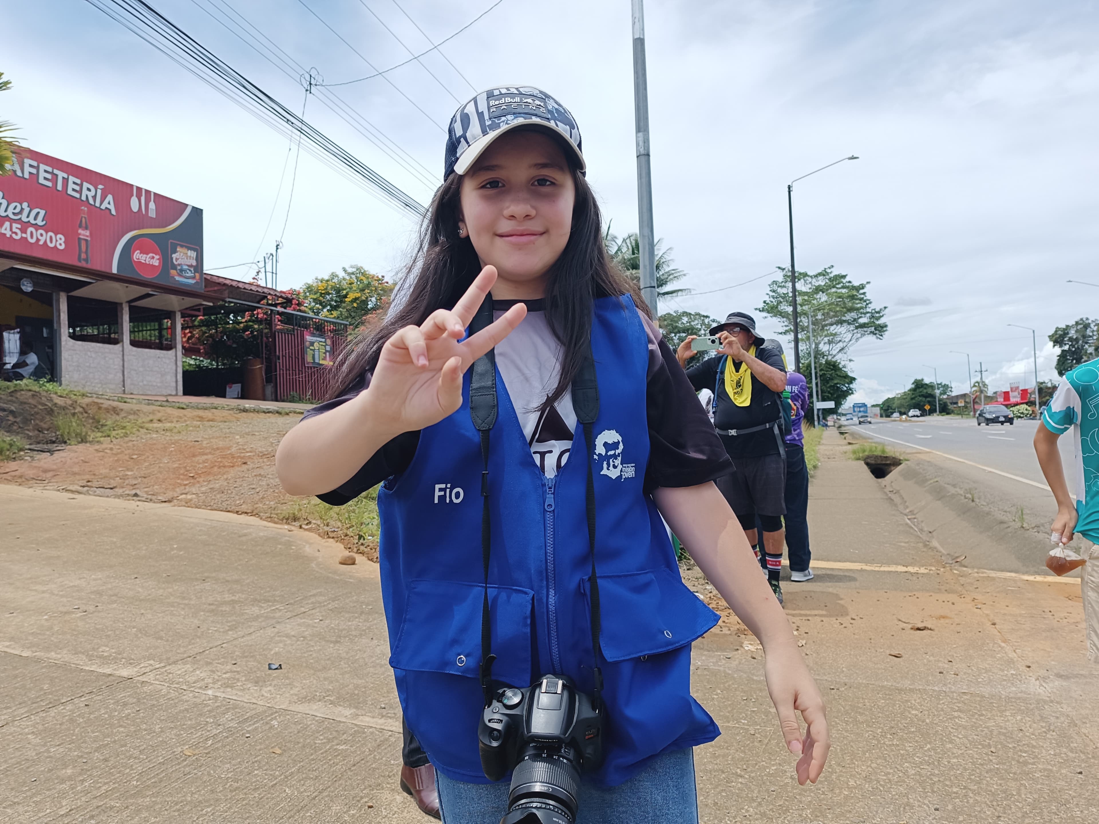 Joven del Equipo de Comunicación Social con chaleco azul y cámara fotográfica durante una actividad
