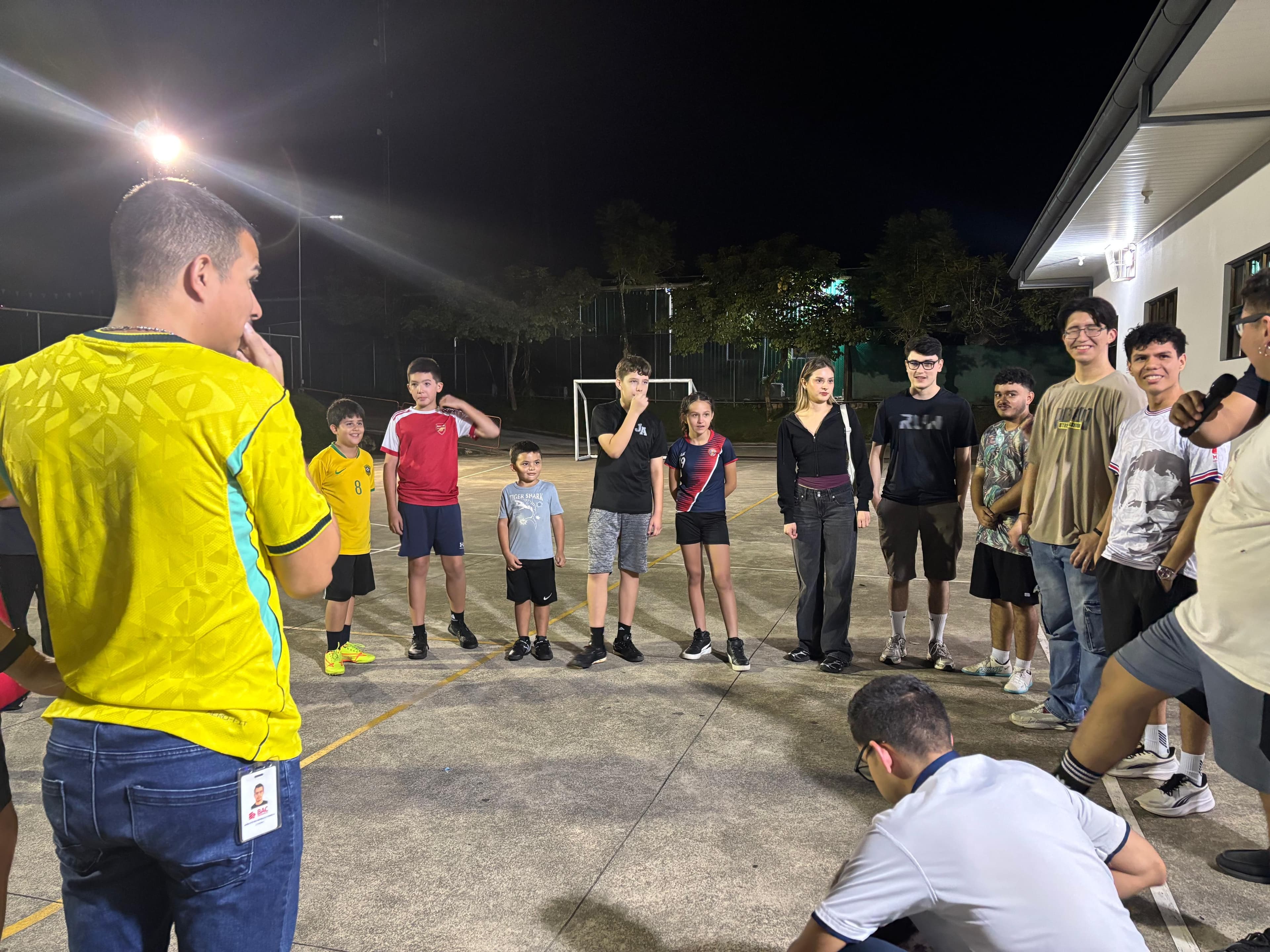 Jóvenes reunidos en círculo en la cancha durante una dinámica recreativa del Oratorio Nocturno.