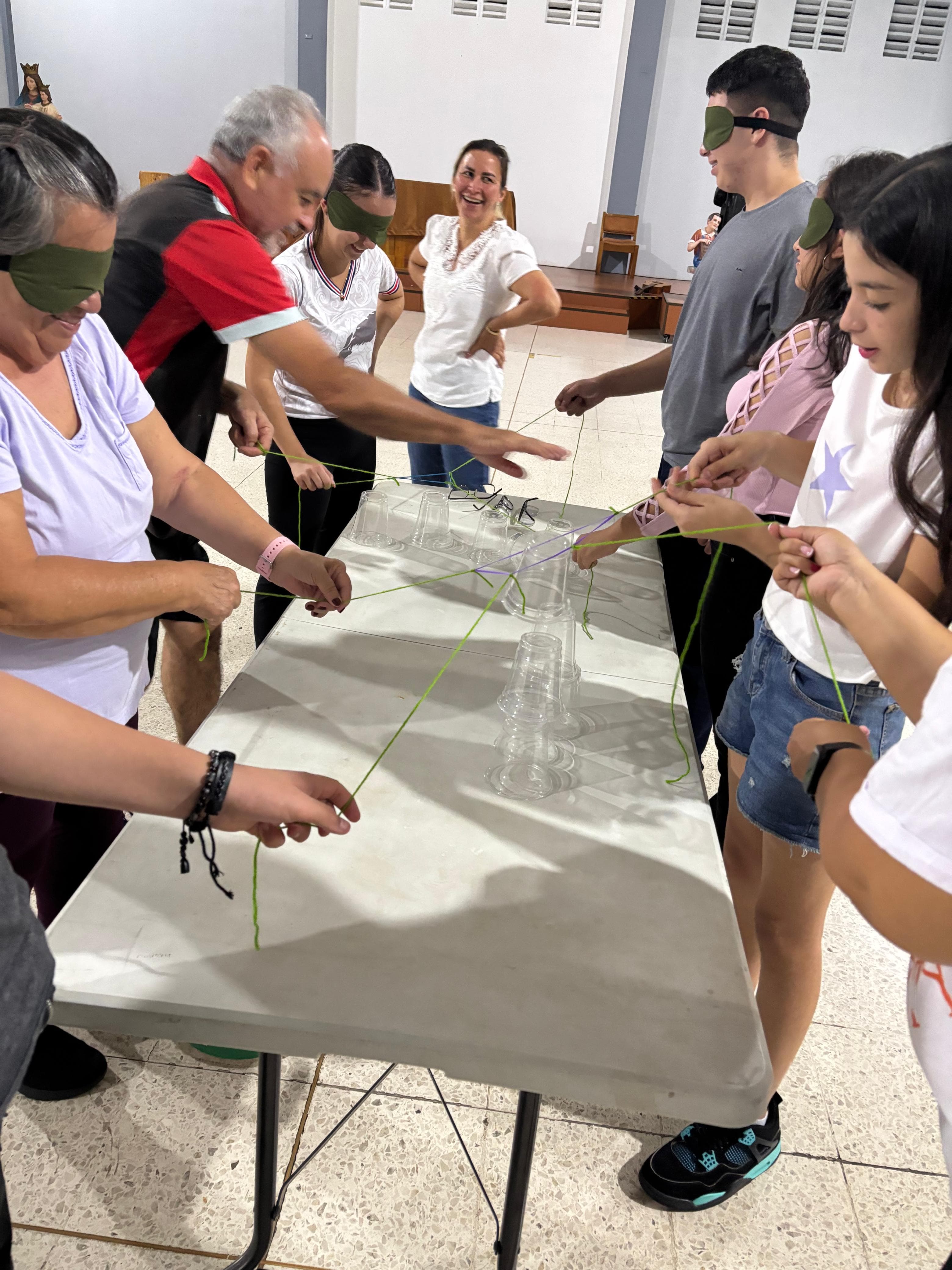 Participantes realizando una dinámica grupal con vasos e hilos durante el Oratorio Nocturno.